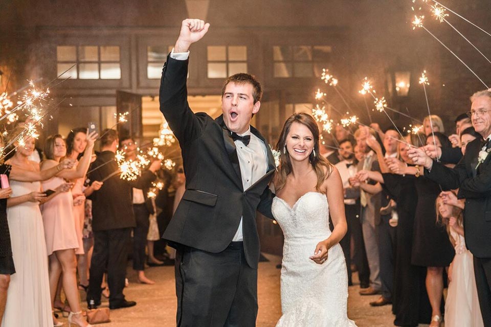 Photo of a bride and groom walking through arch of sparklers outside