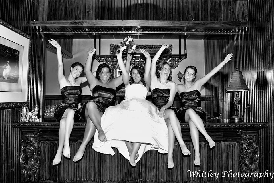 Black and white photo of bridal party sitting on the bar at the Mad Boar