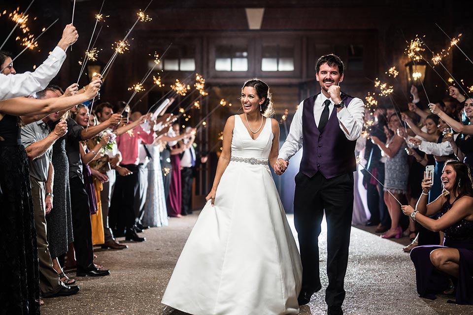 Photo of a bride and groom walking through arch of sparklers outside