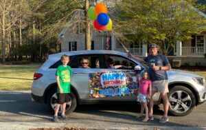 Photo of residents in a car with others people standing around the car